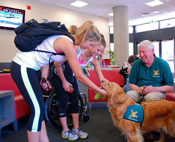 Two women petting therapy dog who's leash is held by it's handler
